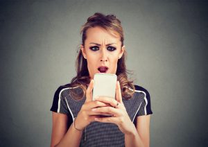 Closeup portrait funny shocked scared woman looking at phone seeing bad news photos message with disgusting emotion on face isolated on gray background.