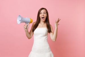 Portrait of excited bride woman with opened mouth in wedding dress holding megaphone, spreading hands isolated on pink pastel background. Organization of wedding concept. Copy space for advertisement.