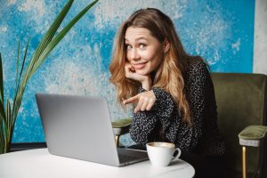 Emotional beautiful young pretty woman sitting in cafe indoors using laptop computer drinking coffee.