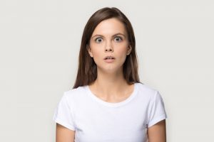 Scared girl looking at camera posing over grey studio background