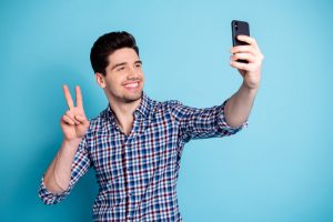 Photo portrait of attractive optimistic crazy funky carefree having free time nice mood v-sign influencer millennial generation y he him guy holding using telephone in hand isolated pastel background