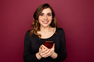 Female exited person holding red mobile standing indoor on the pink background.