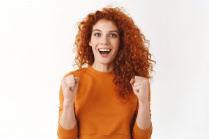 Excited gorgeous redhead girlfriend rooting for favorite team. Curly girl clench fists motivated and ambitious, smiling broadly, cheering, triumphing watching football game, celebrate win and success