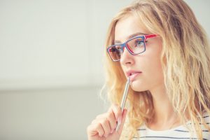 University student girl pensive with pen on her lips. Portrait of thinking woman with glasses.